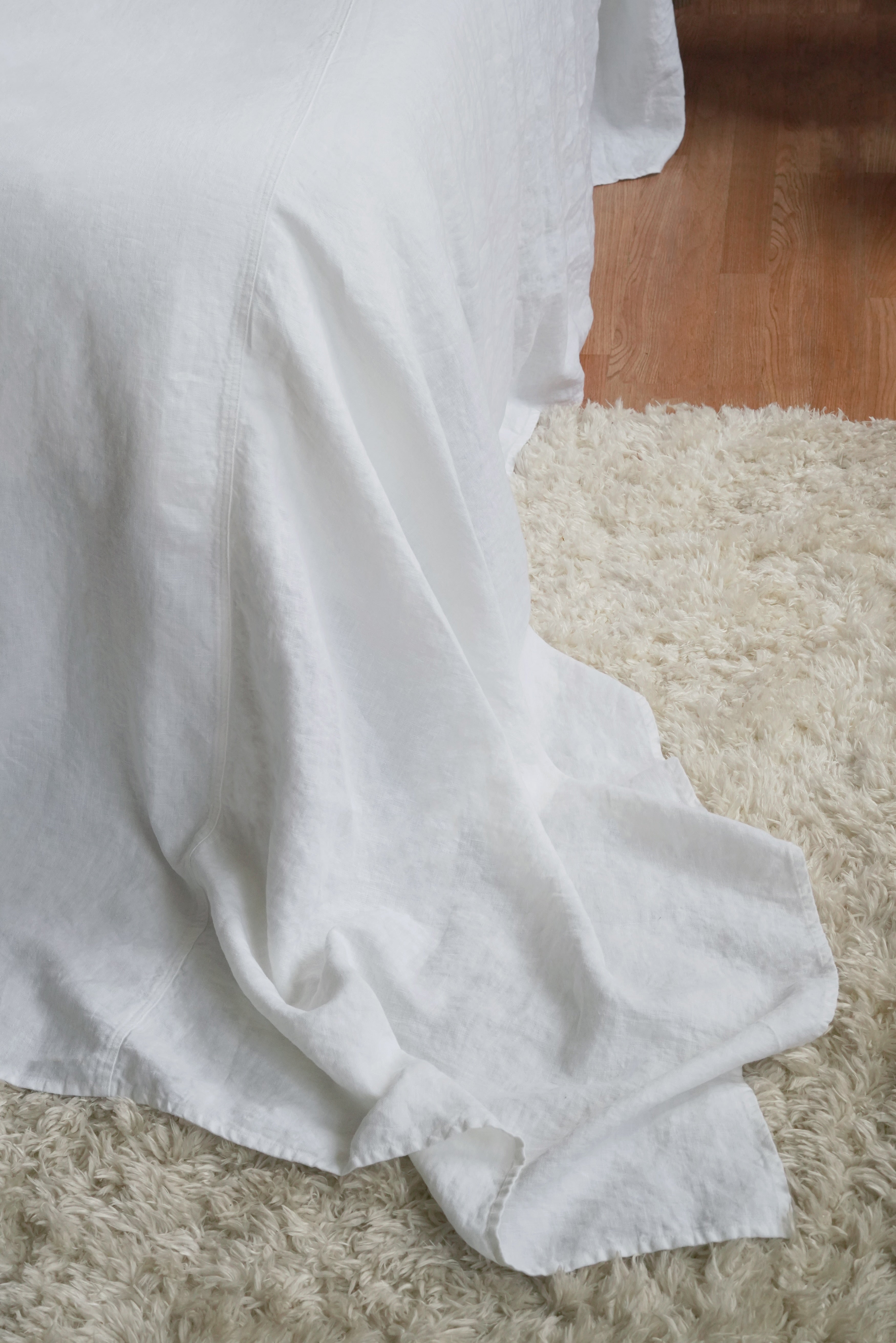Detail shot of white linen bedding "puddling" on the floor, perfect for Japandi and modern coastal bedroom decor